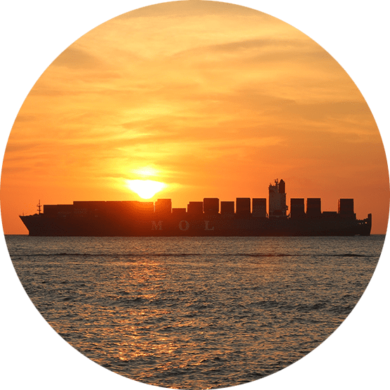 Large cargo ship in the ocean, with orange sky and sun setting.