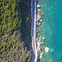 Aerial view of a tropical sea with a road running along the water and green trees.