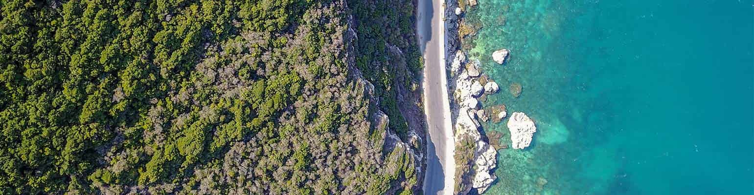 Aerial view of a tropical sea with a road running along the water and green trees.